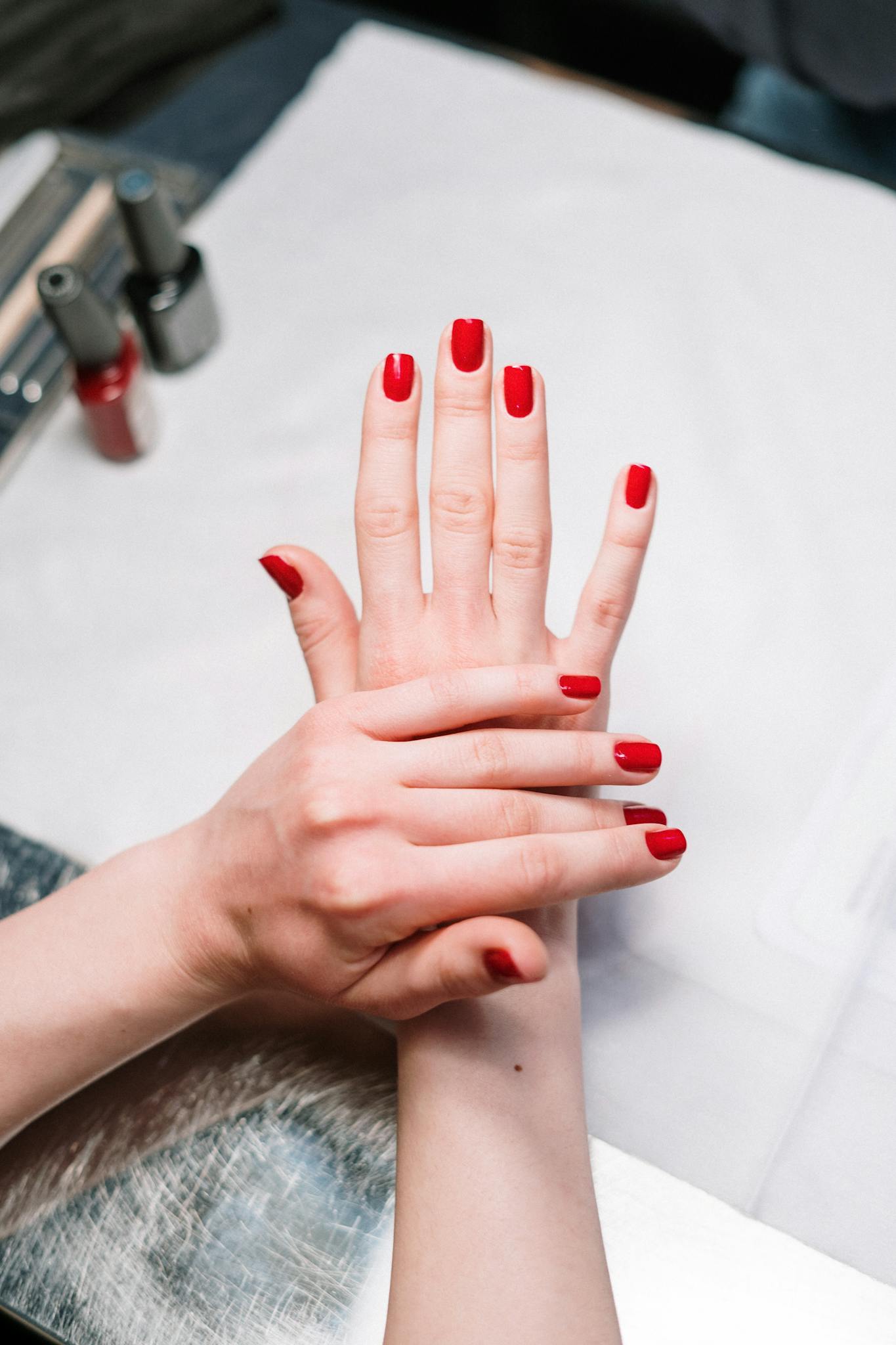 Close-up of elegant red nail polish on hands in a salon setting, showcasing modern manicure art.